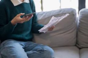 persona fa i conti sul telefono leggendo la bolletta
