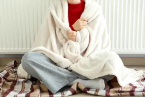 Giovane donna seduta a terra avvolta nella coperta davanti al termosifone