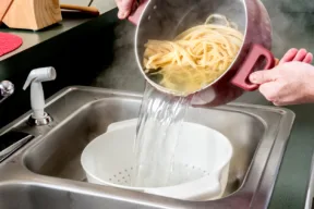 persona che butta l'acqua della pasta nel lavandino