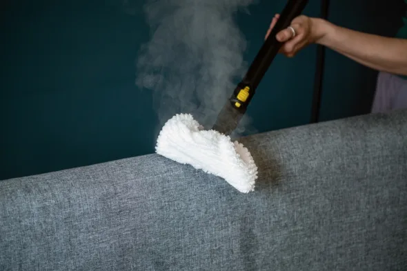 persona pulisce divano con scopa a vapore