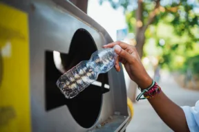 una persona getta la bottiglia di plastica nel bidone